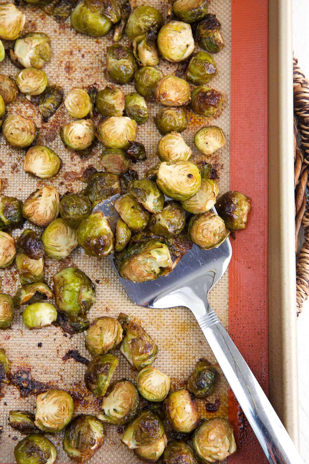 A spatula is lifting a small portion of brussel sprouts from a baking sheet.