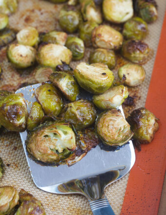 Brussel sprouts are being slightly lifted from the baking sheet with a metal spatula.