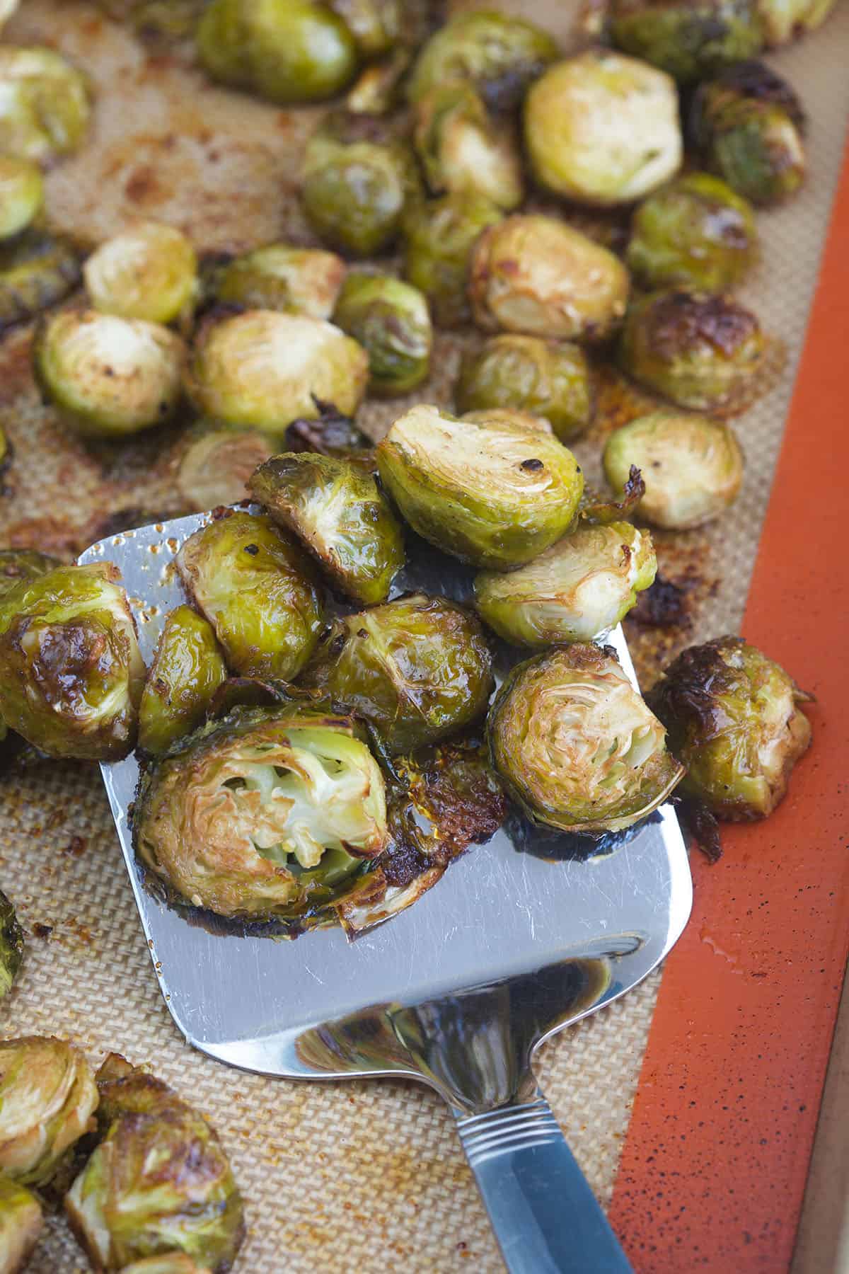 Brussel sprouts are being slightly lifted from the baking sheet with a metal spatula. 