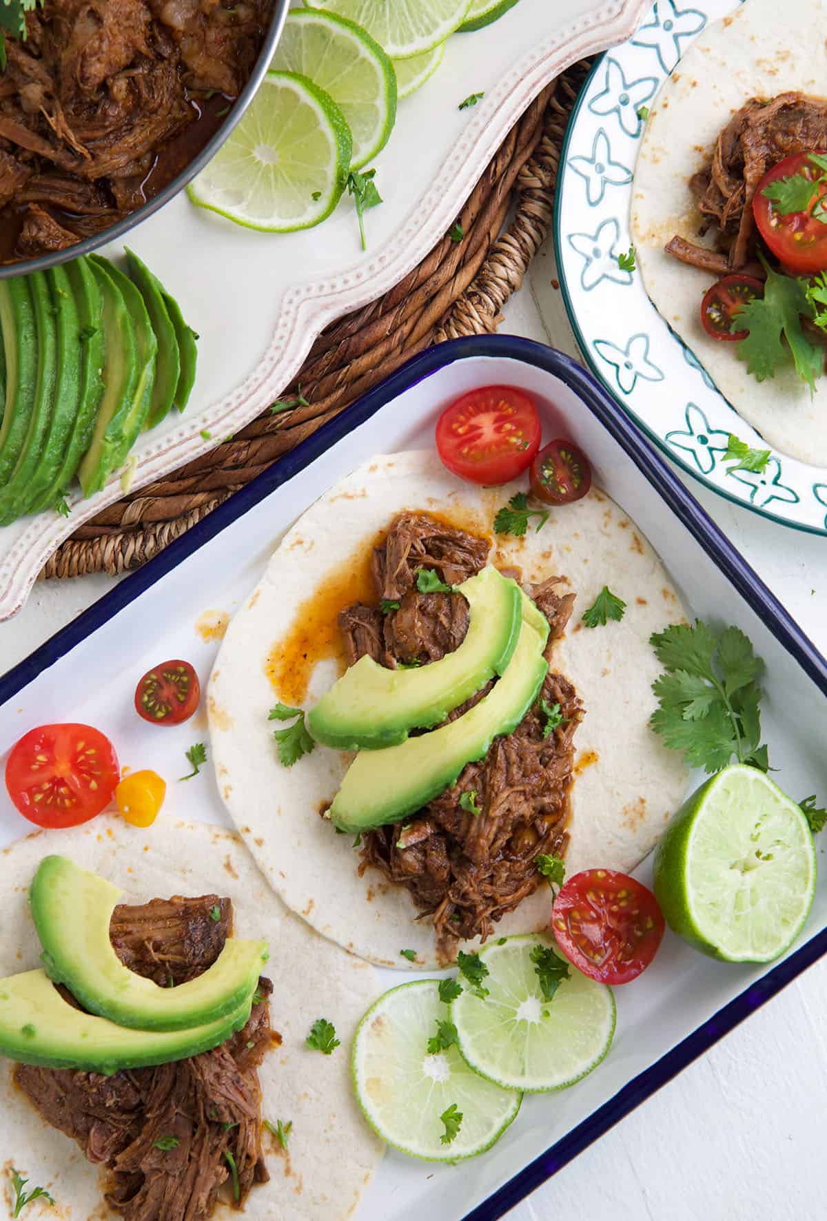 Several beef barbacoa tacos are garnished with avocado slices. 