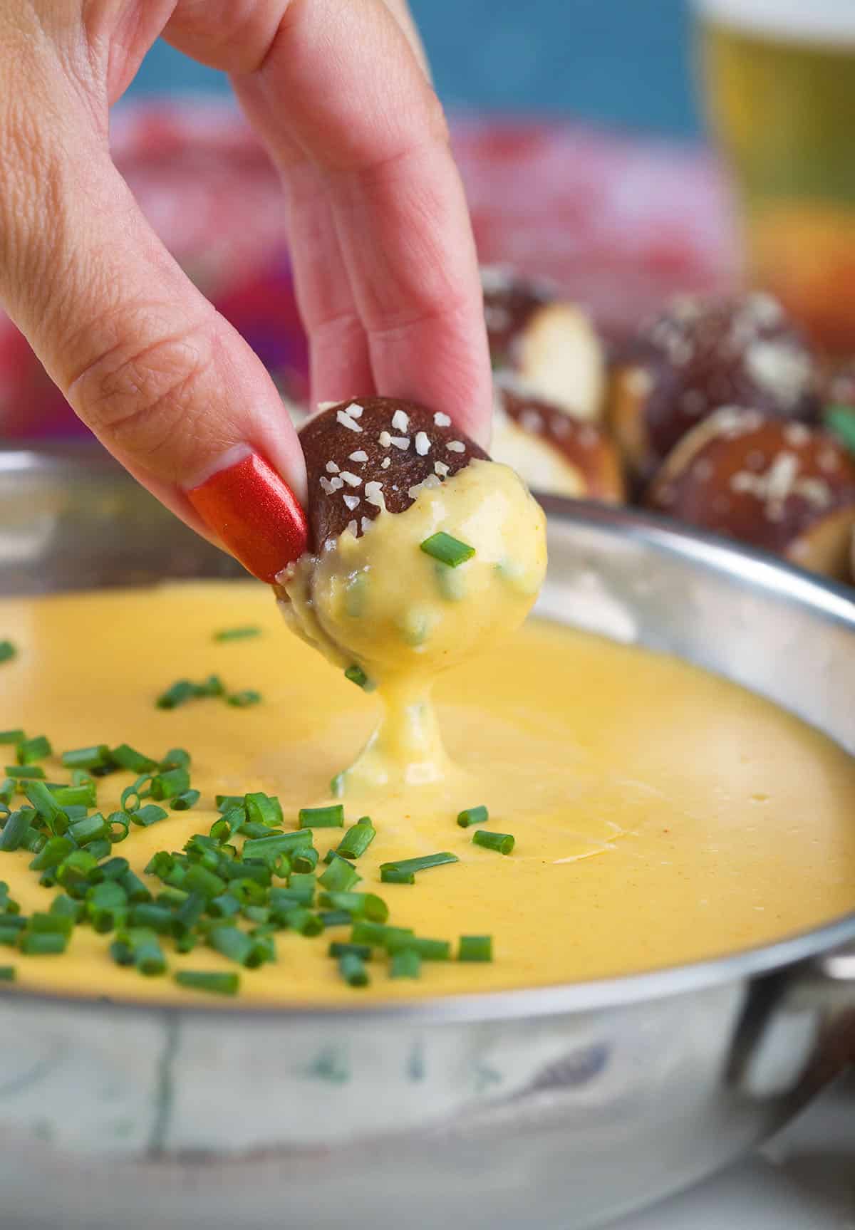 A soft pretzel bite has been dipped in beer cheese sauce.