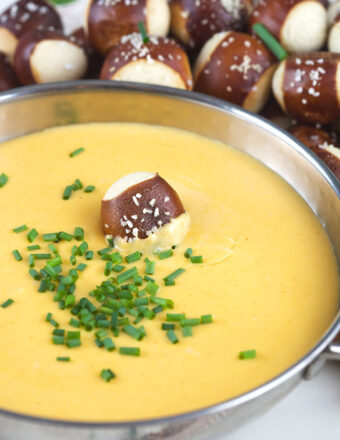 Chopped chives and one soft pretzel bite garnish a bowl of cheese dip.