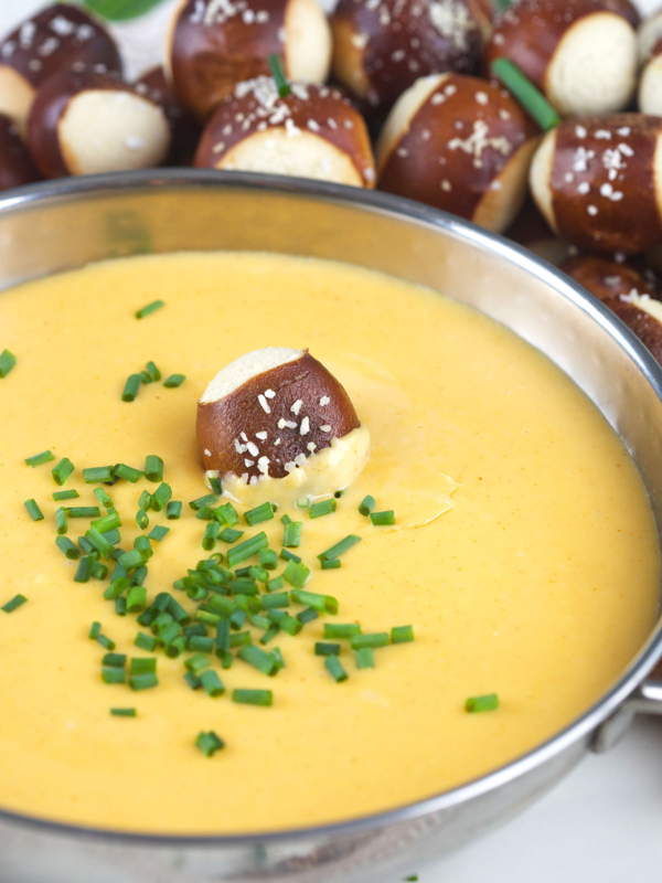 Chopped chives and one soft pretzel bite garnish a bowl of cheese dip.