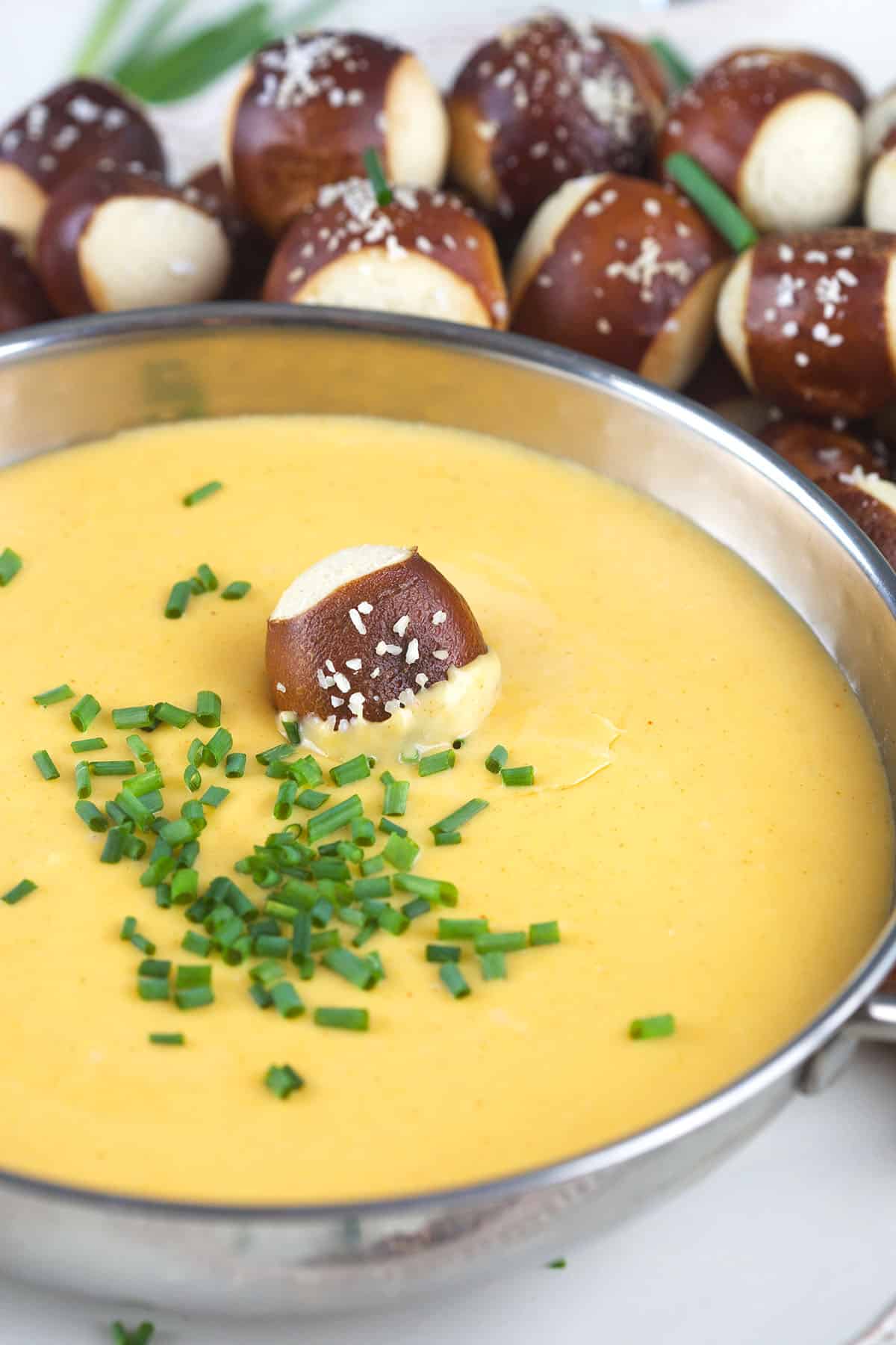 Chopped chives and one soft pretzel bite garnish a bowl of cheese dip.