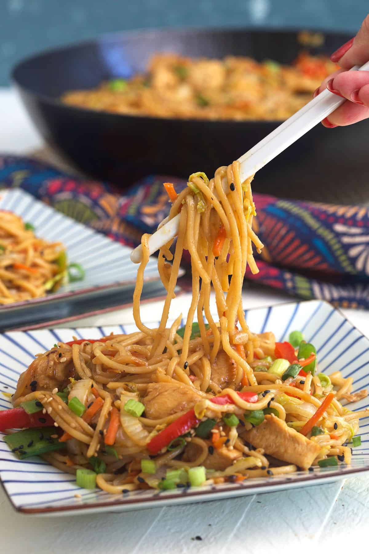 Noodles are being lifted from a plate with a pair of chopsticks. 