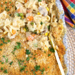 A serving spoon is lifting up a small portion of chicken noodle casserole from the dish.