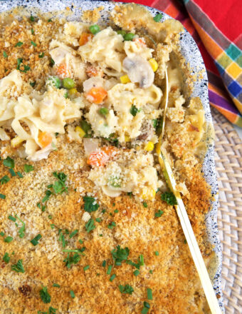 A serving spoon is lifting up a small portion of chicken noodle casserole from the dish.
