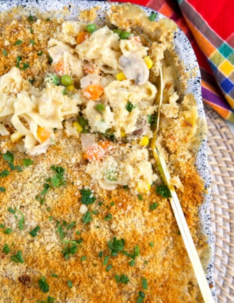 A serving spoon is lifting up a small portion of chicken noodle casserole from the dish.