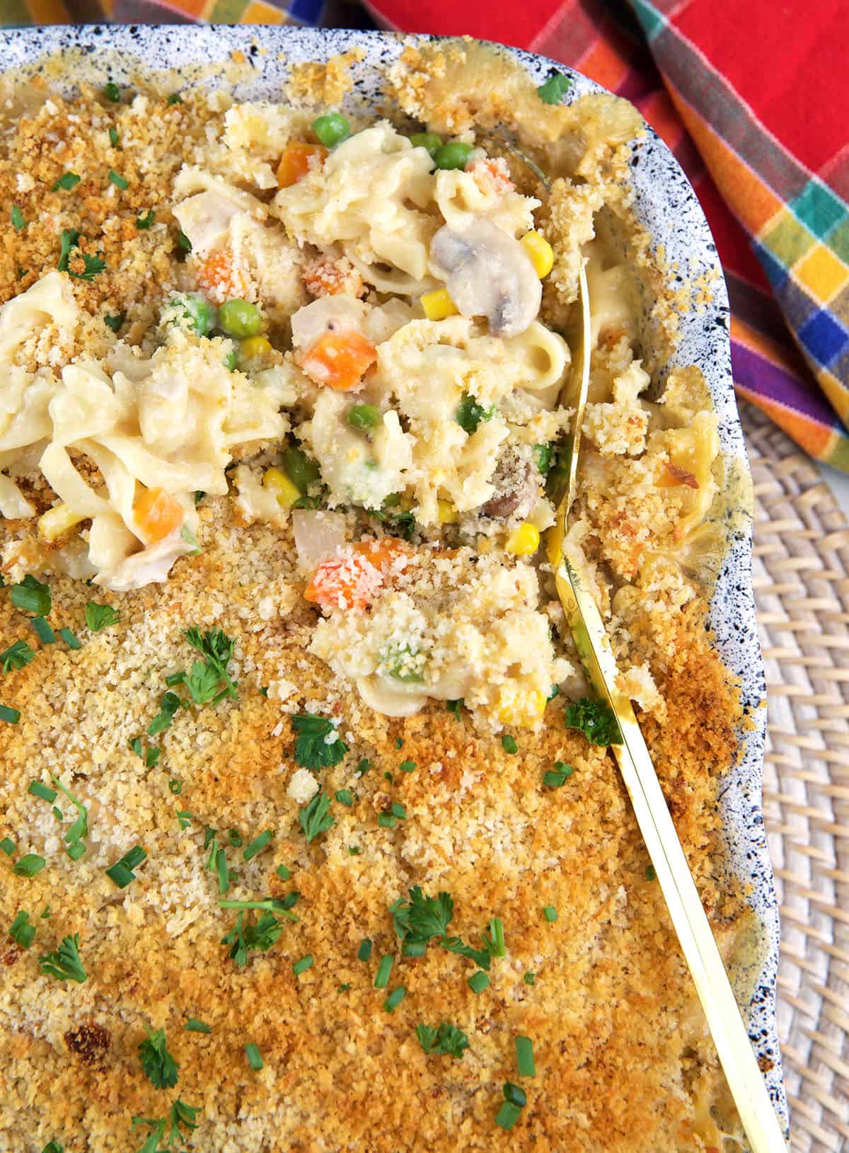 A serving spoon is lifting up a small portion of chicken noodle casserole from the dish.
