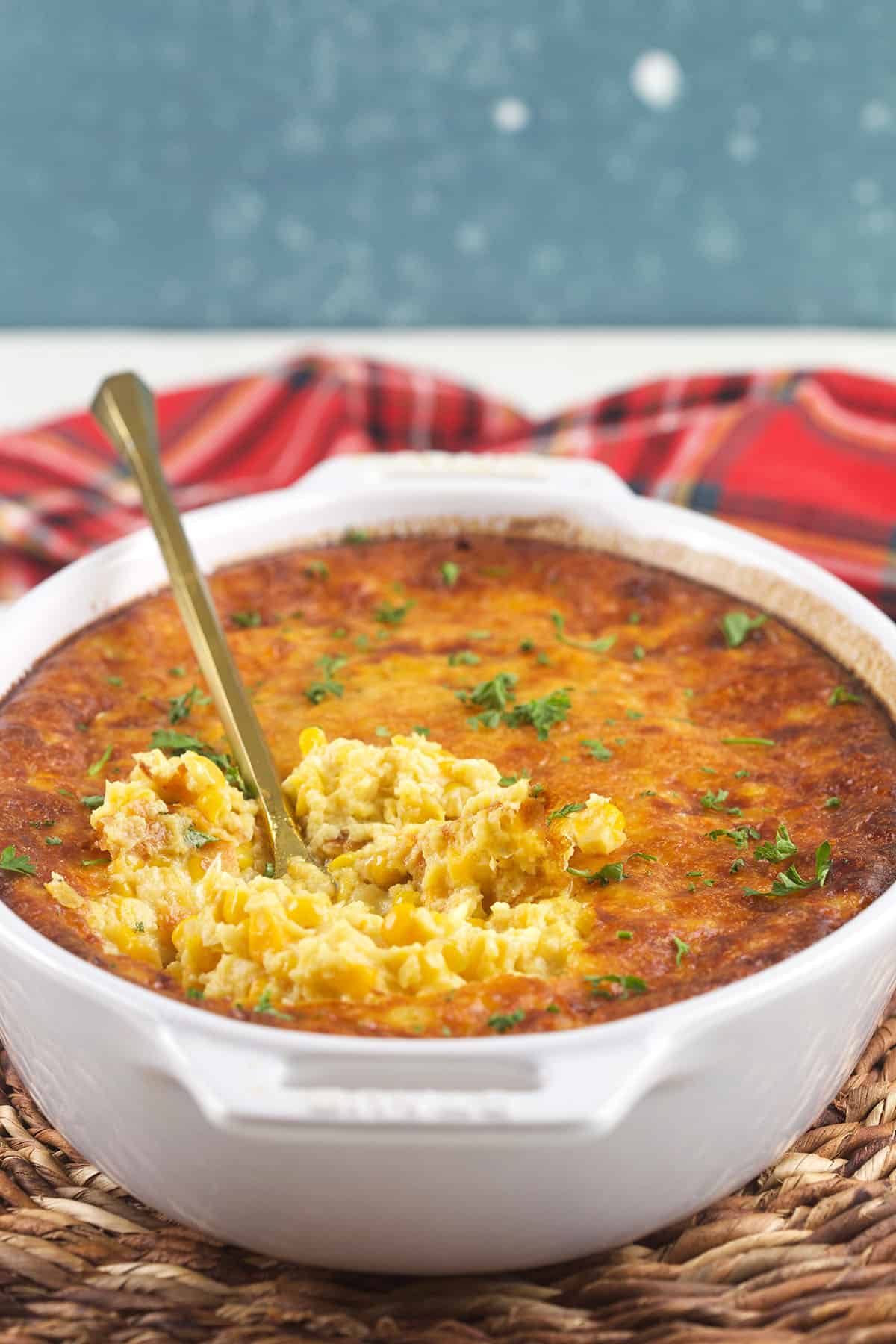 A serving spoon is placed in a casserole dish filled with baked corn pudding. 