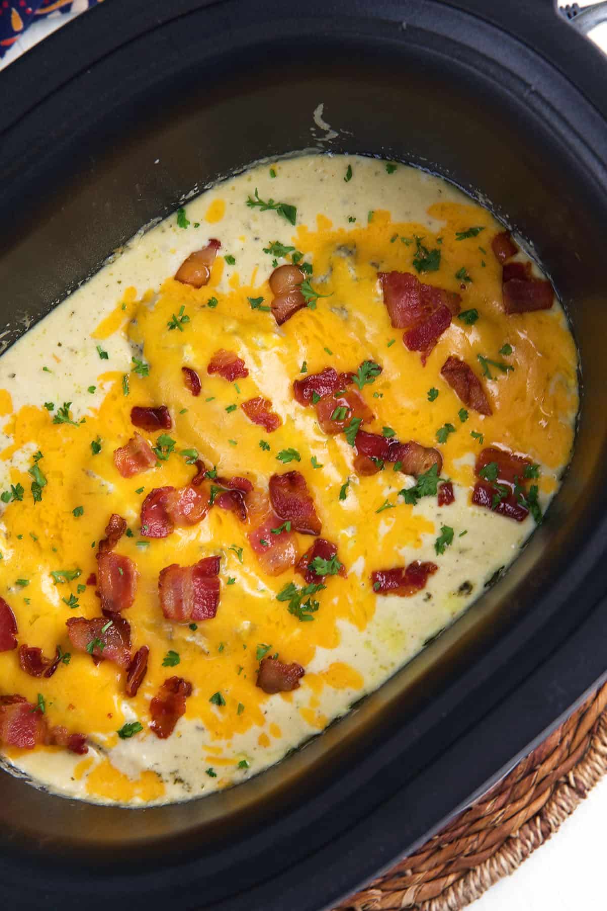 Cheese and bacon top a serving of crack chicken that's still in the slow cooker. 