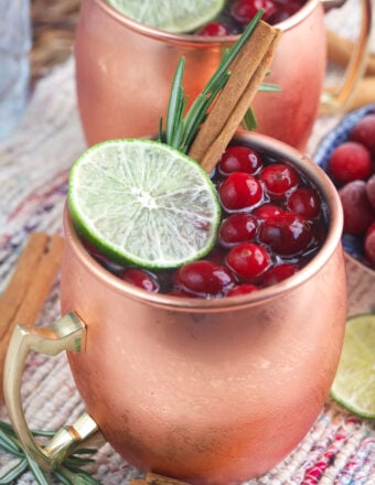 A garnished cranberry moscow mule is presented in a copper mug.