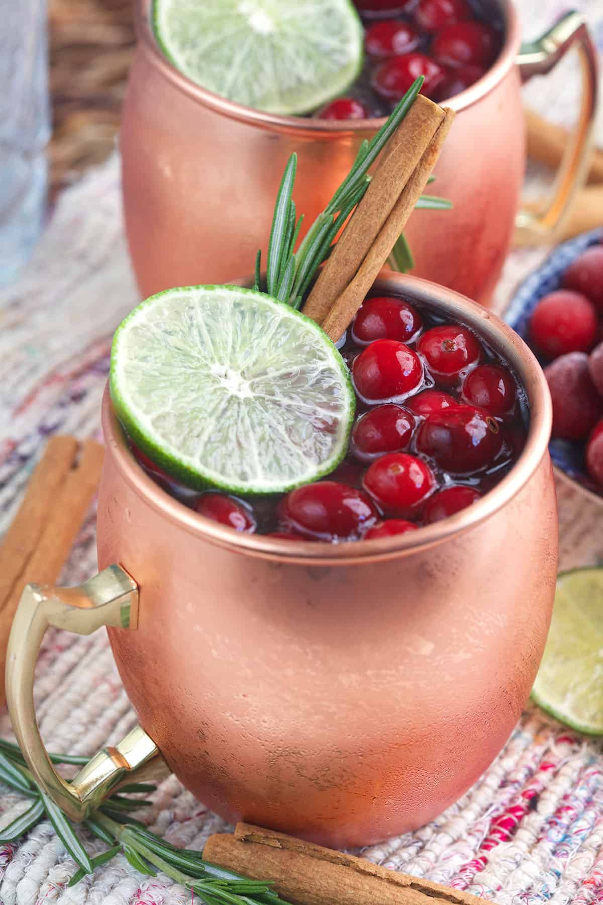 A garnished cranberry moscow mule is presented in a copper mug.