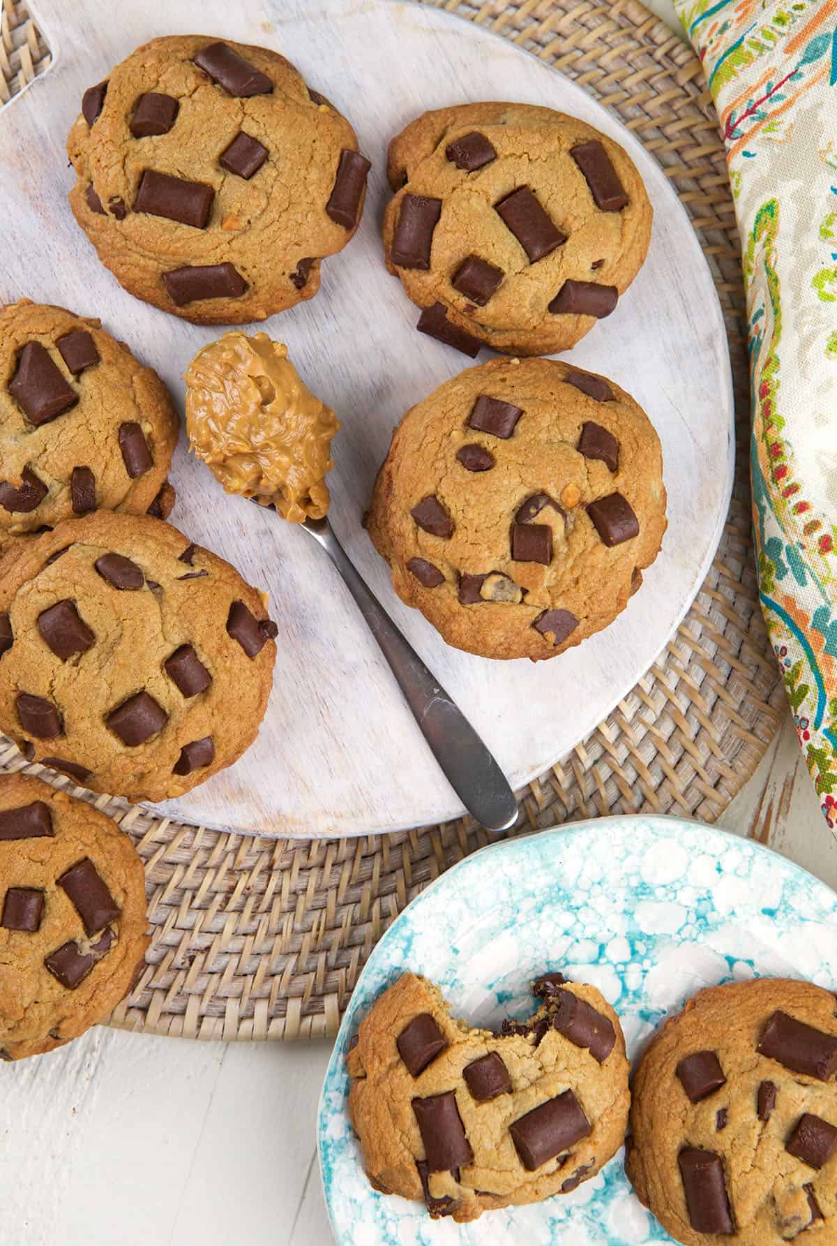 A spoon with peanut butter on it is placed next to a batch of peanut butter chocolate chip cookies. 