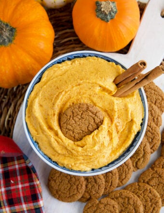 A garnished bowl of pumpkin dip is placed next to real pumpkins.