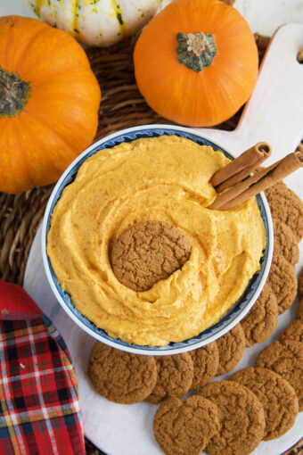 A garnished bowl of pumpkin dip is placed next to real pumpkins.