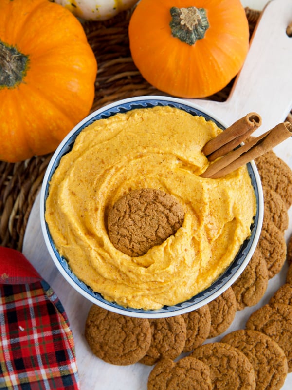 A garnished bowl of pumpkin dip is placed next to real pumpkins.