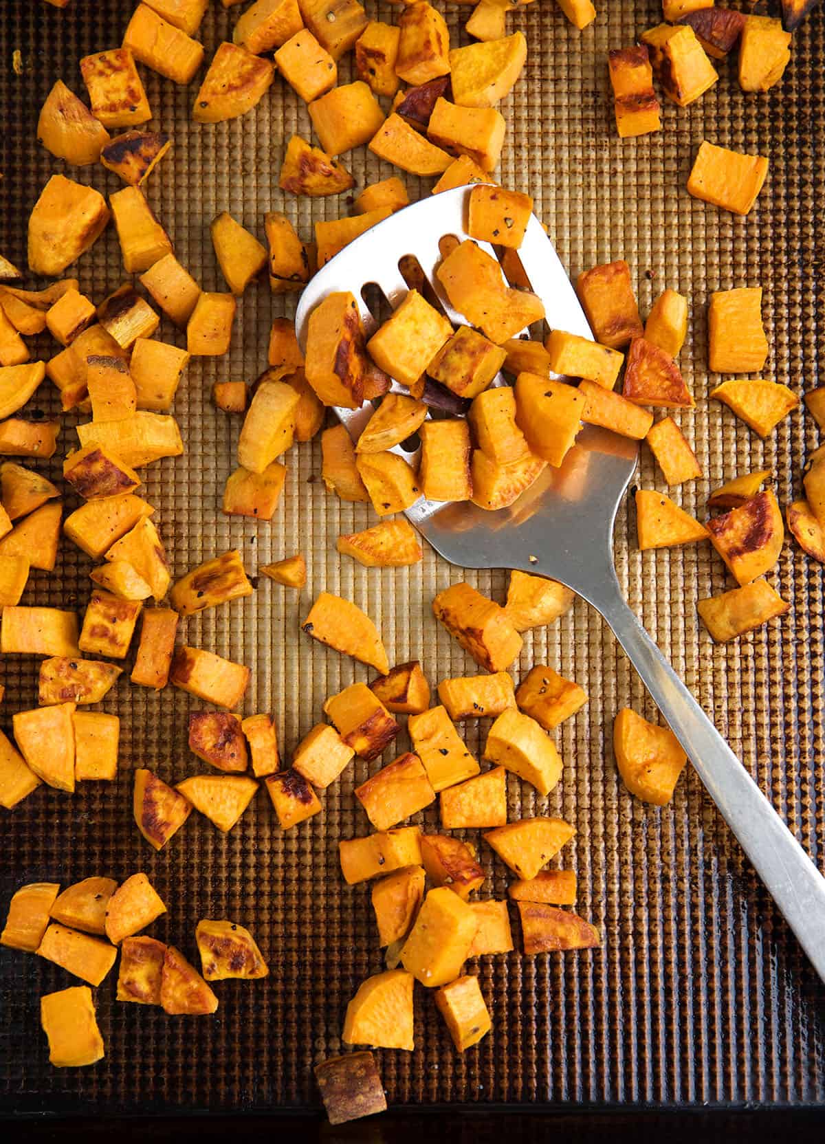 A spatula is lifting some roasted sweet potatoes from a baking sheet.