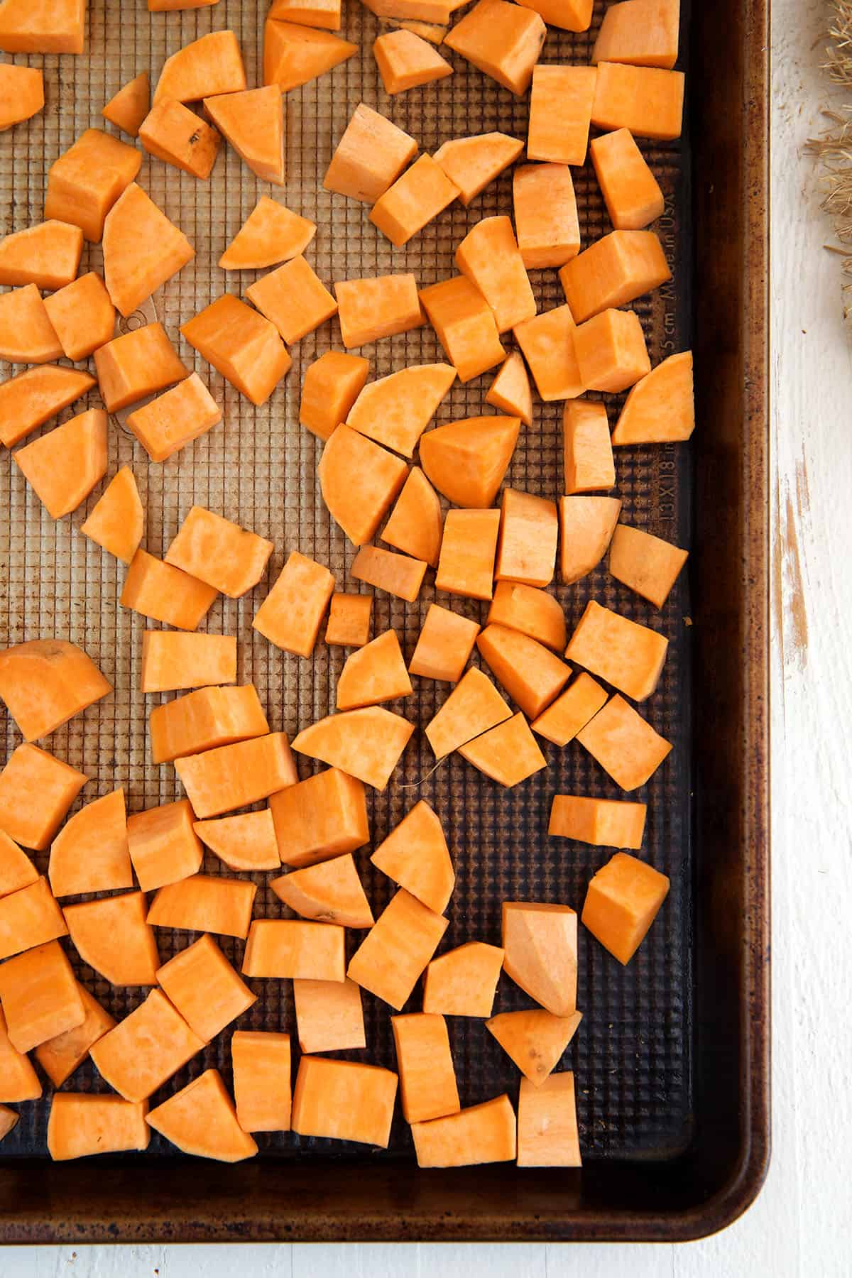 Uncooked sweet potato chunks are spread out on a baking sheet. 