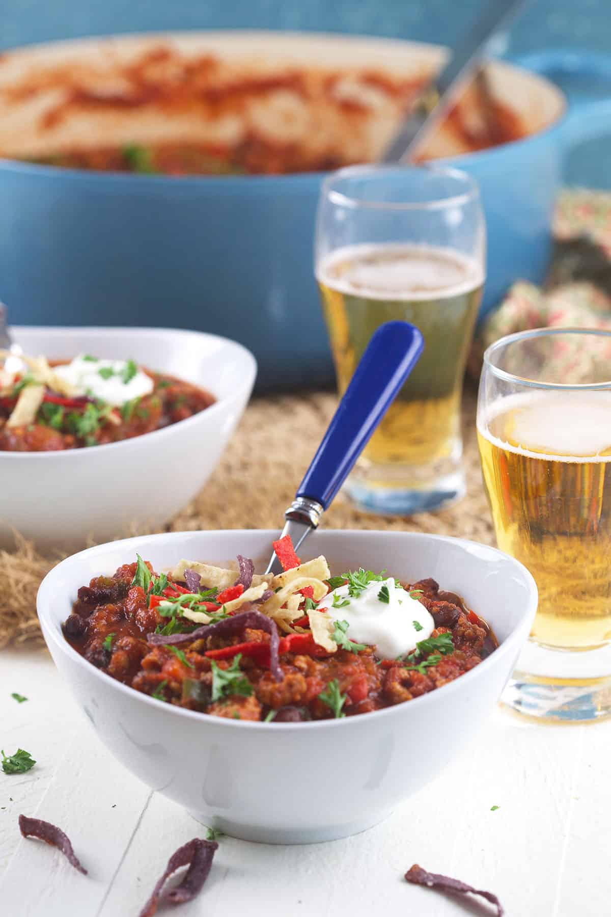 A single serving of turkey chili is placed next to two glasses of beer. 