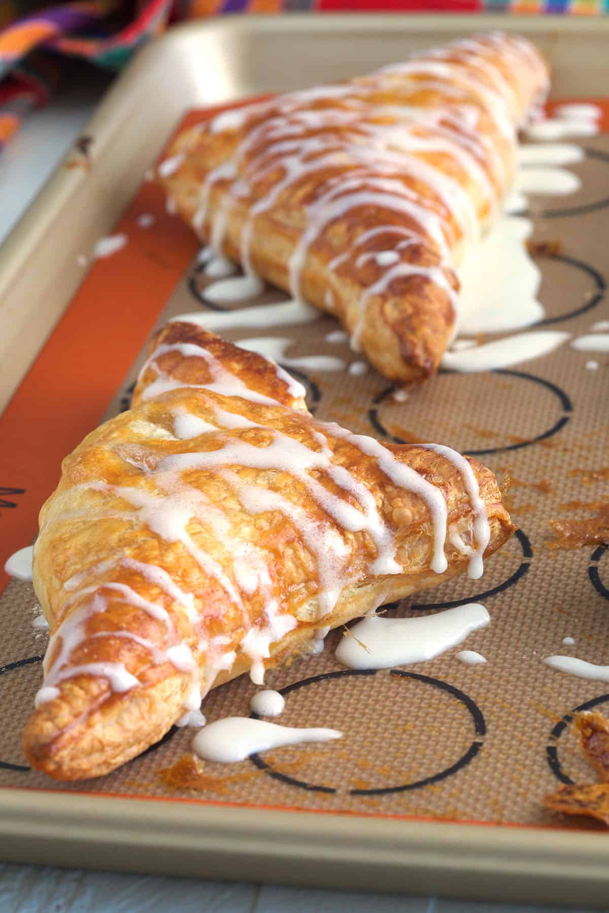 Glazed turnovers are spread out on a baking sheet. 