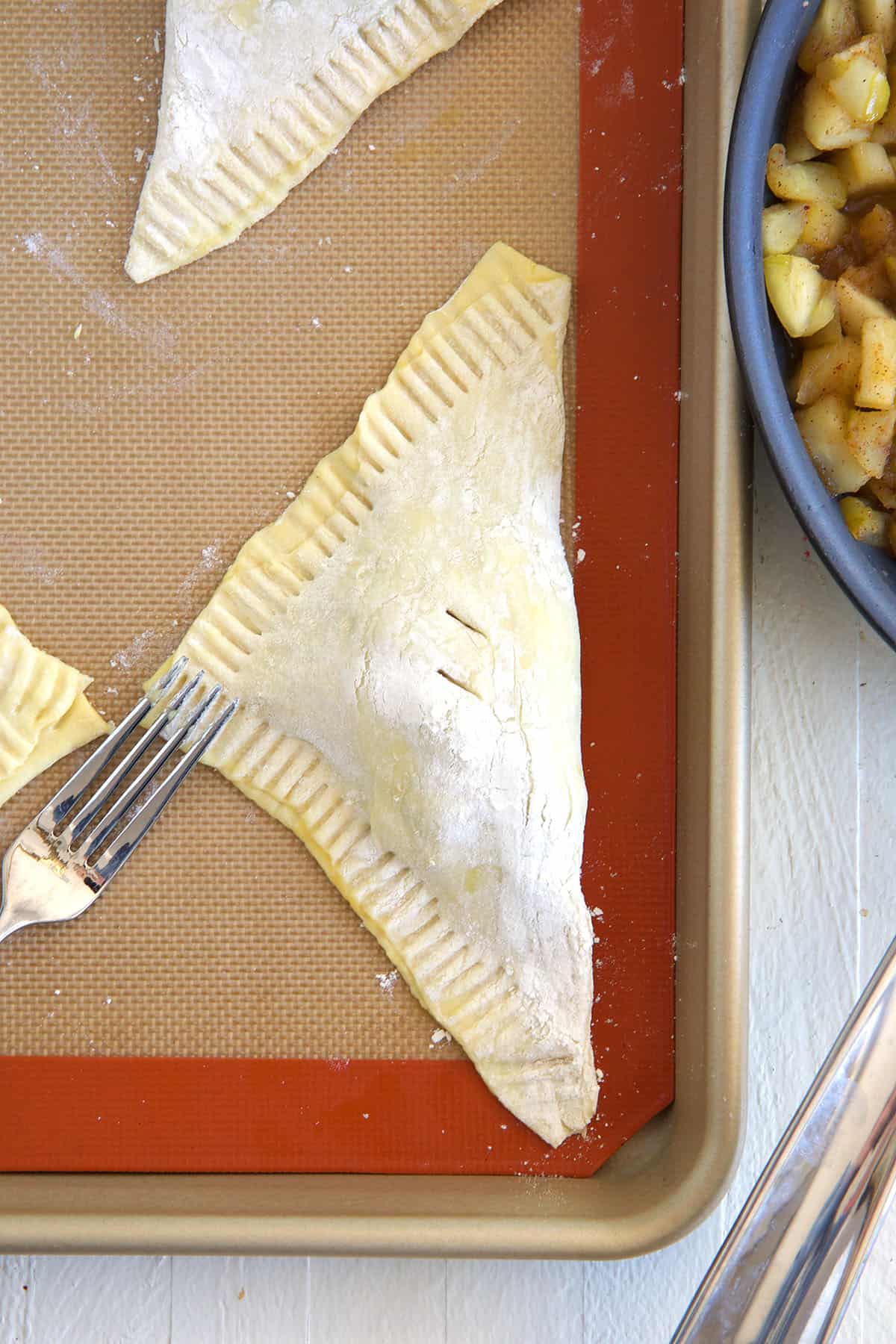 An uncooked apple turnover is being crimped with a fork. 