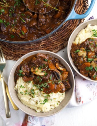 Two bowls of beef bourguignon are placed next to a full skillet.