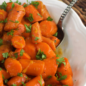 A white bowl is filled with candied carrots.