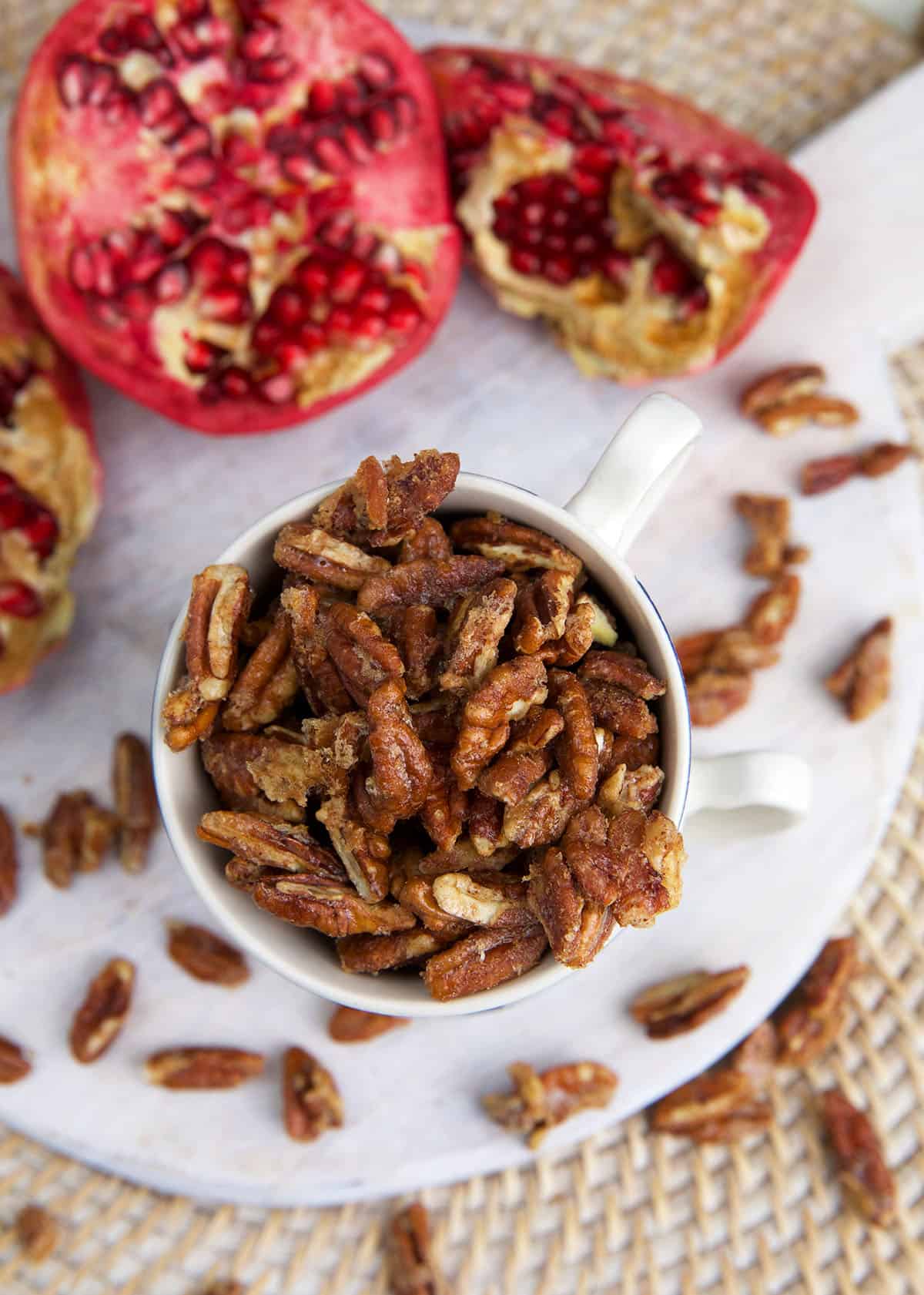 A pomegranate is placed next to a cup of candied pecans