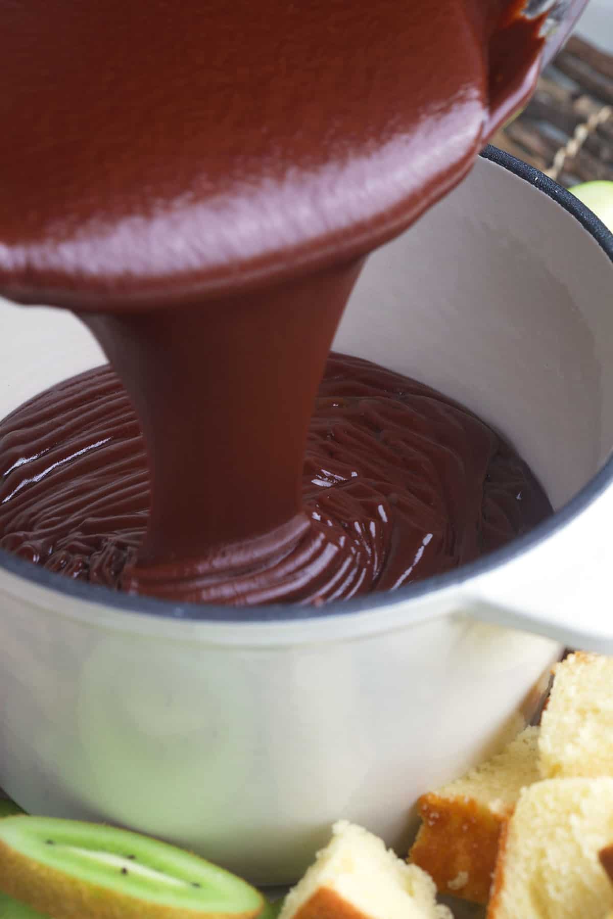 Fondue is being poured into a large pot. 