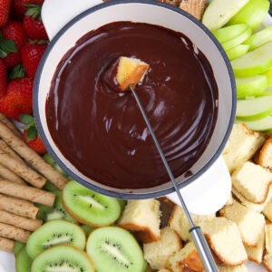 A large bowl of chocolate fondue is placed in the middle of a serving tray full of dippers.