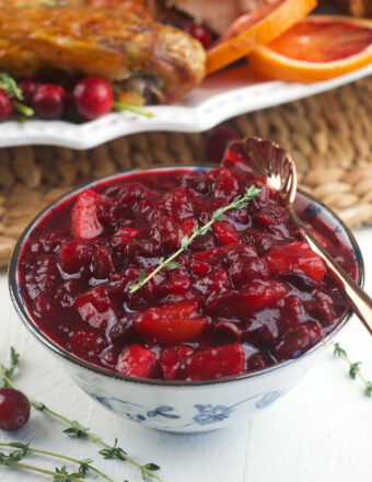 A bowl of cranberry chutney is placed on a white surface.
