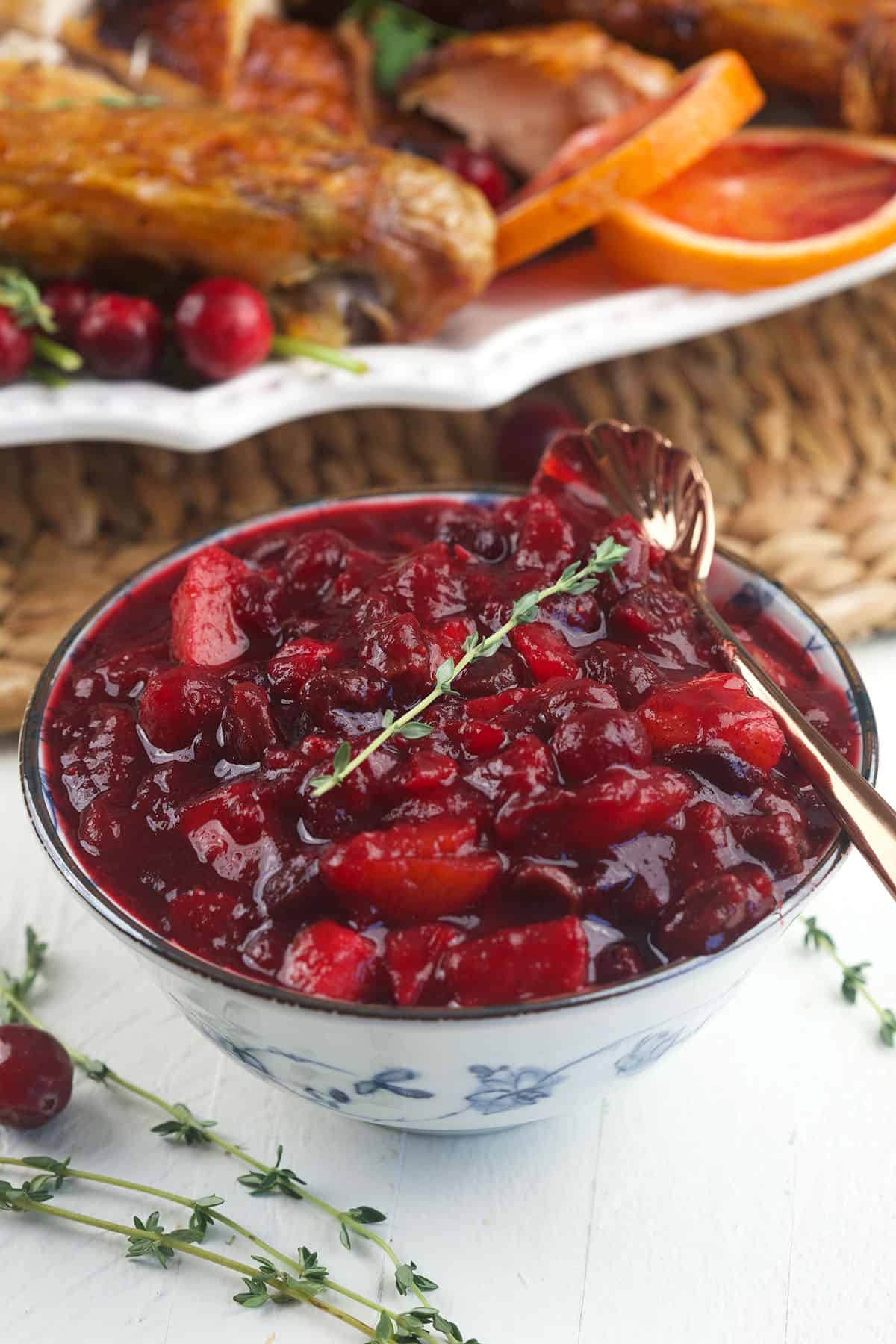 A bowl of cranberry chutney is placed on a white surface. 