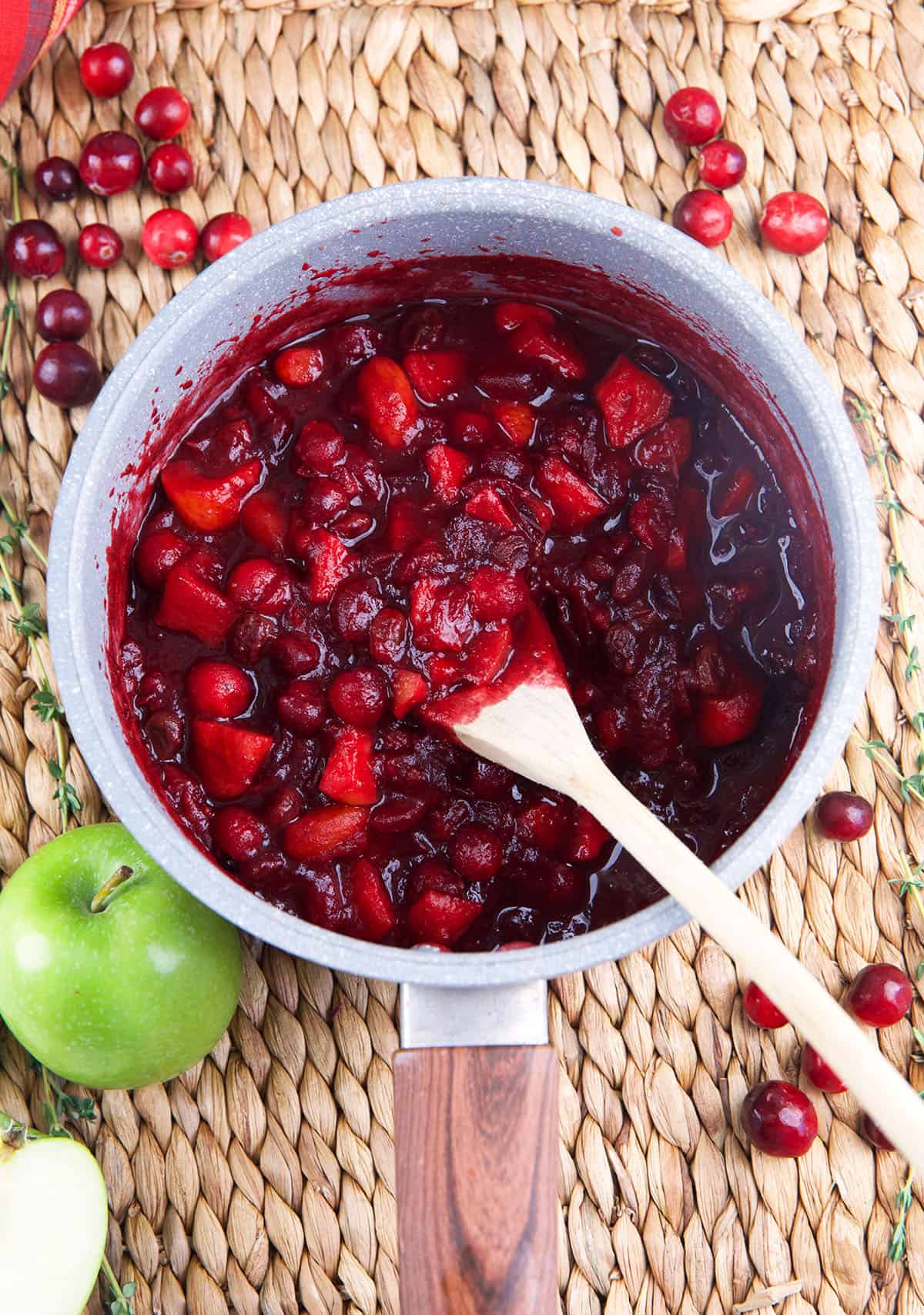 Cranberry chutney is being cooked in a pot and stirred with a spoon. 