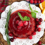A cranberry jello salad is garnished with herbs and berries.