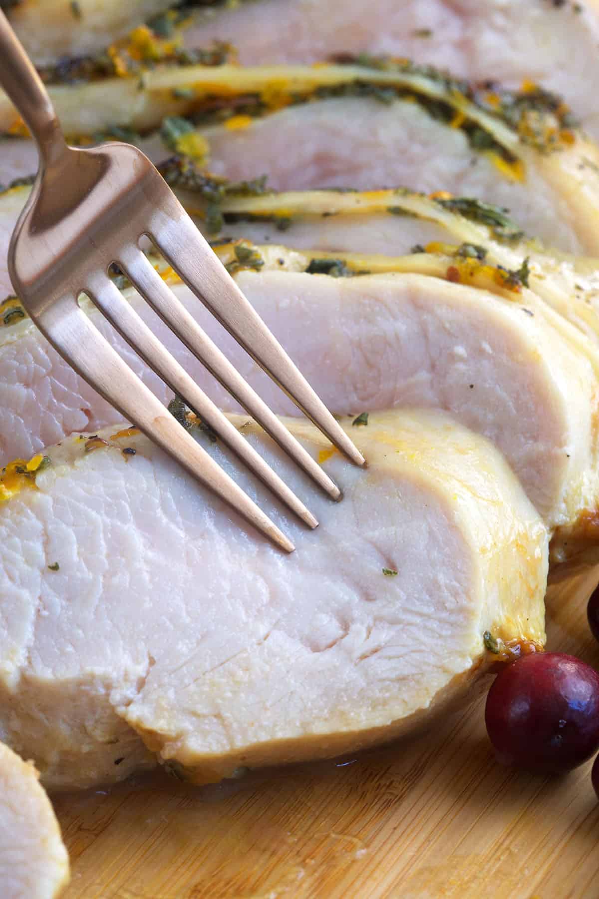 A fork is piercing a piece of roasted turkey breast. 