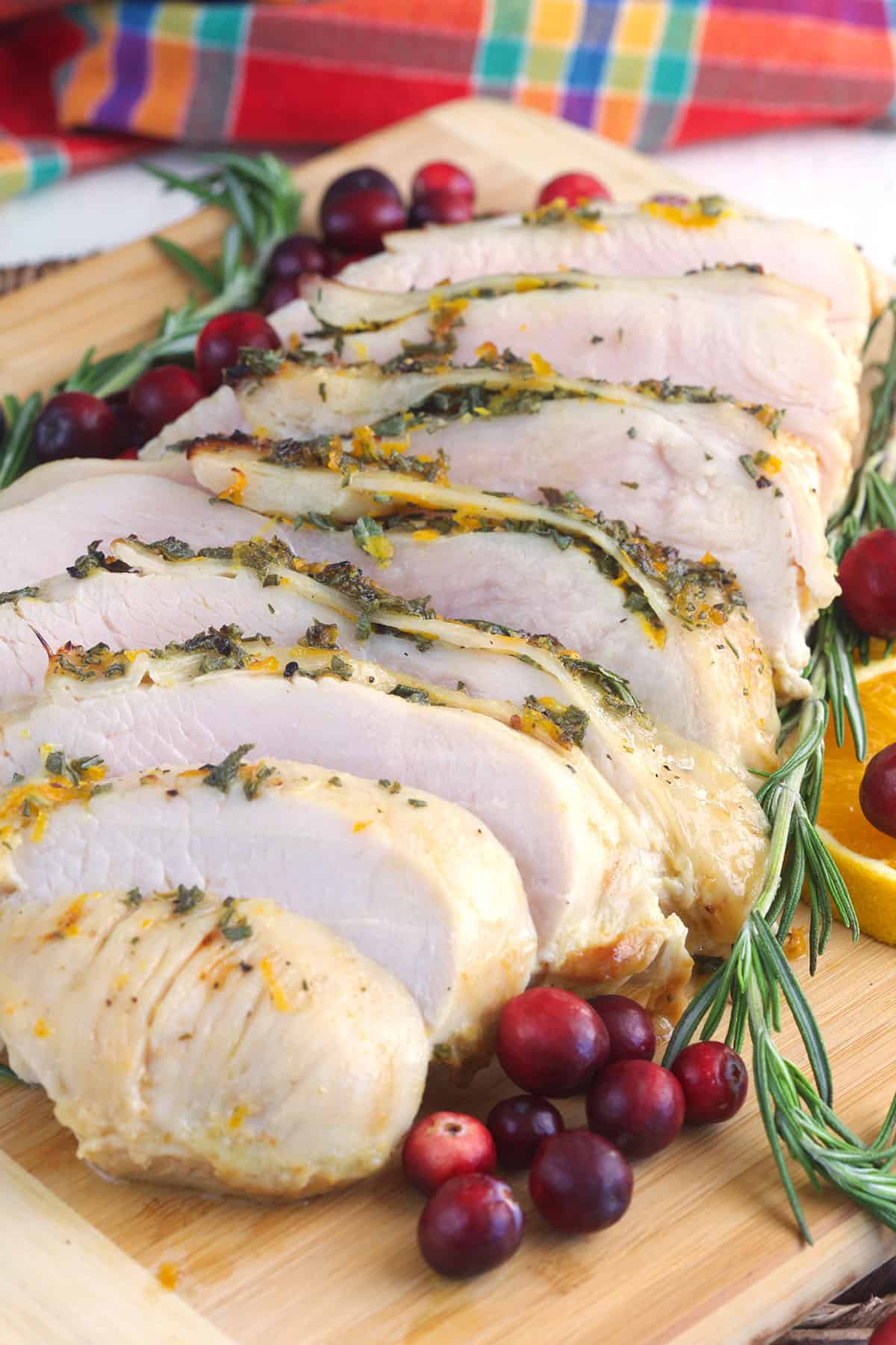 A sliced turkey breast is presented next to cranberries and herbs. 