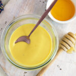 A small bowl full of honey mustard is placed next to a small bowl of honey.
