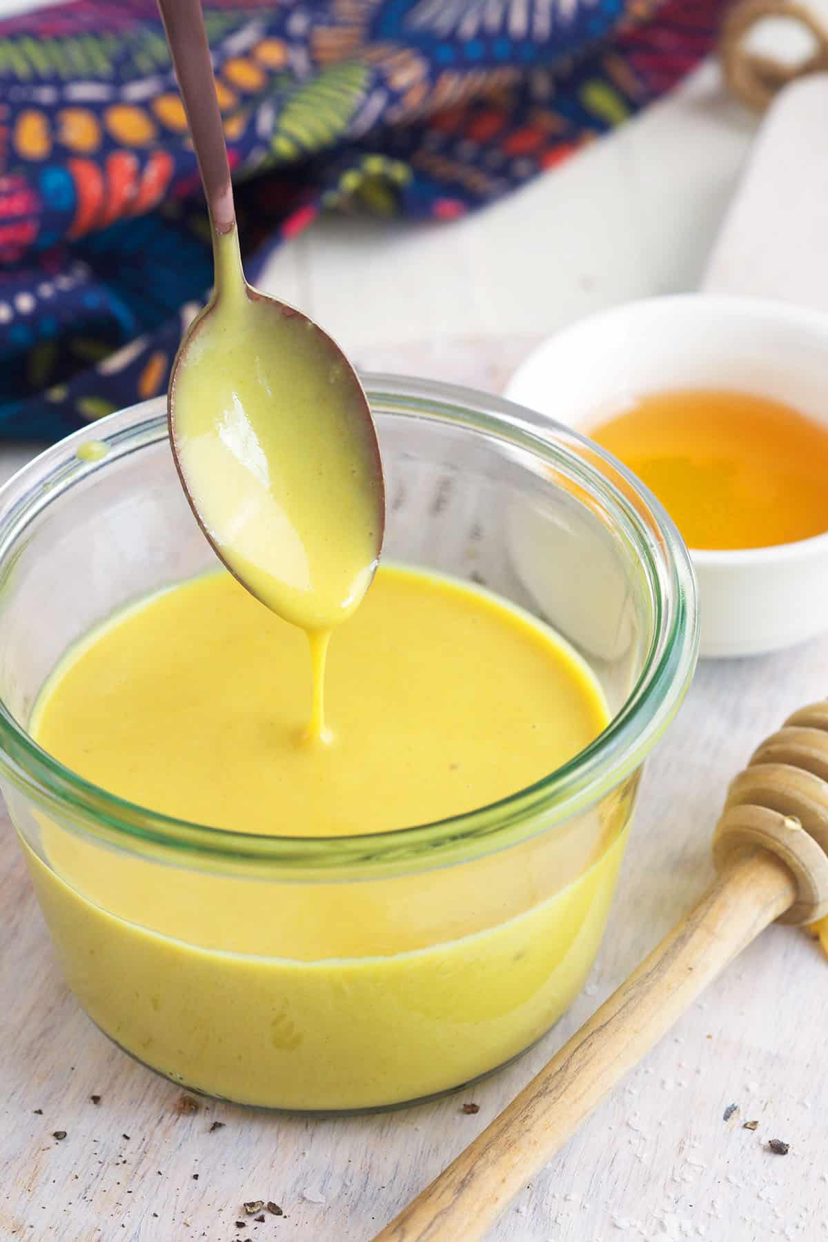 Honey mustard is being drizzled into a small bowl with a spoon. 