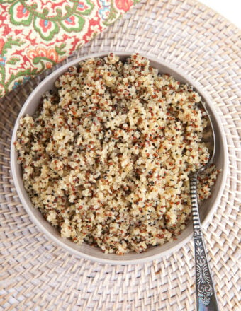 A bowl filled with cooked quinoa is placed on a woven placemat.