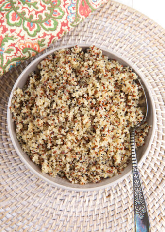 A bowl filled with cooked quinoa is placed on a woven placemat.