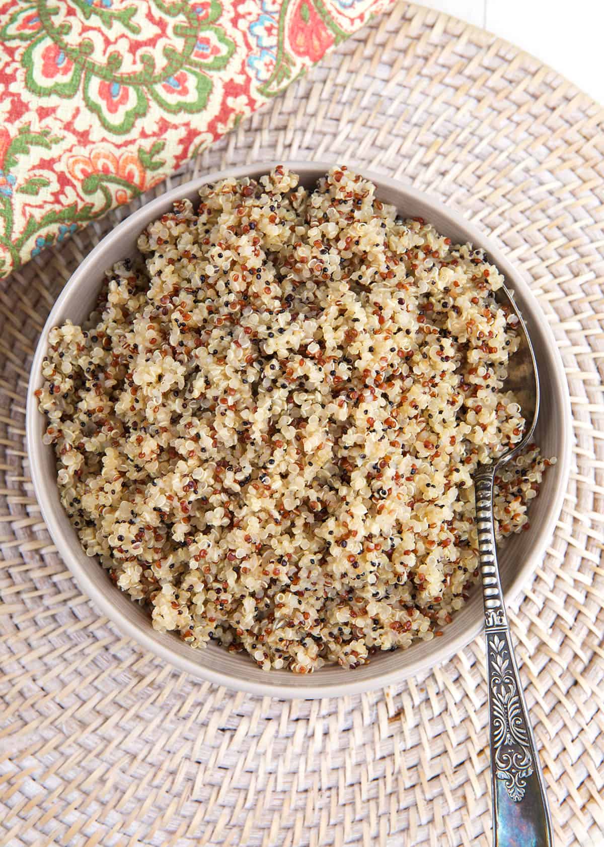 A bowl filled with cooked quinoa is placed on a woven placemat. 