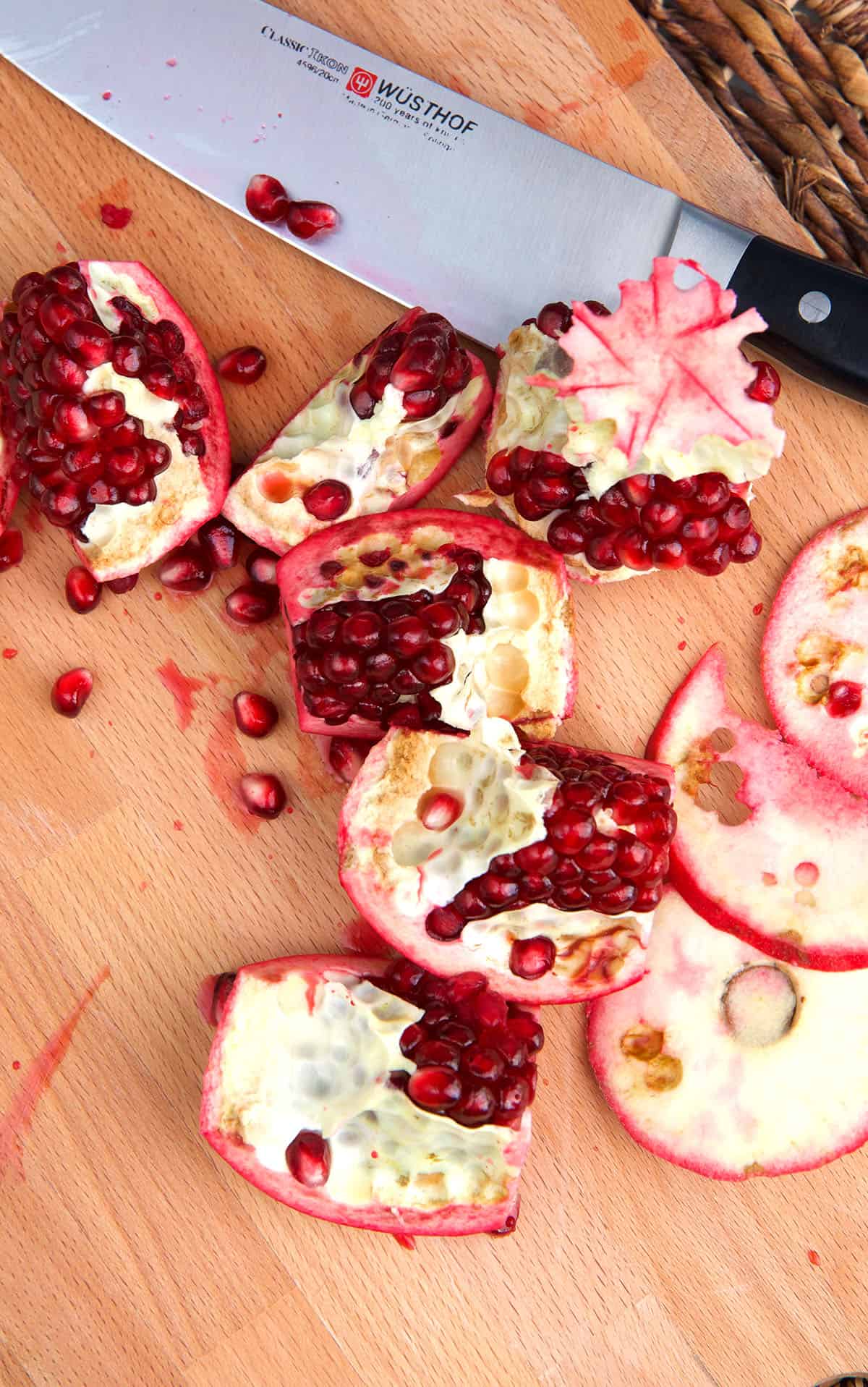 A sliced pomegranate is spread out on a cutting board next to a knife. 