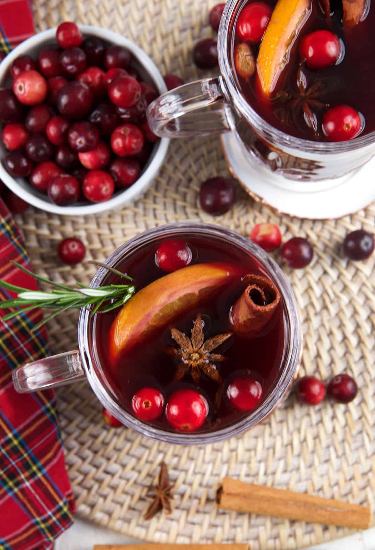 Two glasses of mulled wine are placed next to a bowl of cranberries. 
