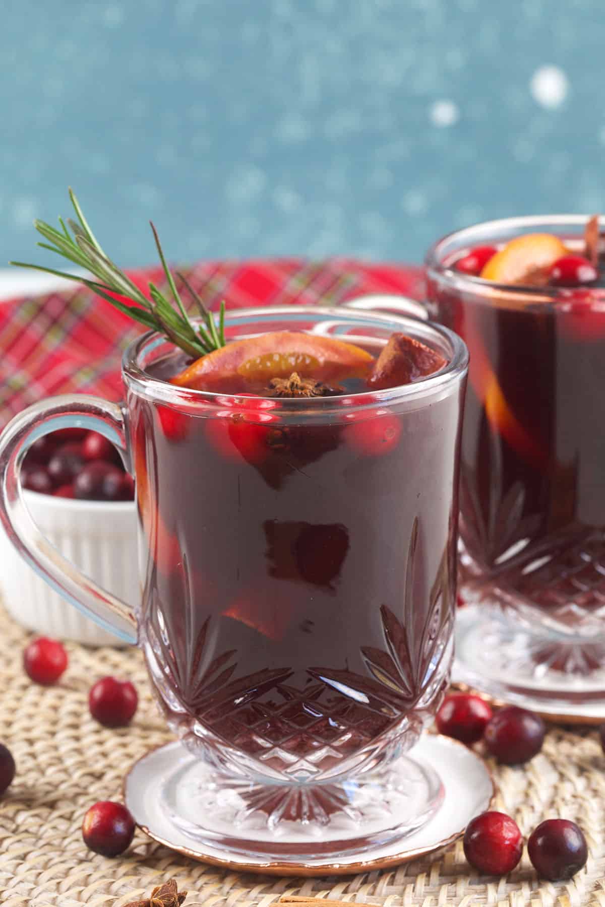 A garnished glass of mulled wine is placed next to cranberries. 