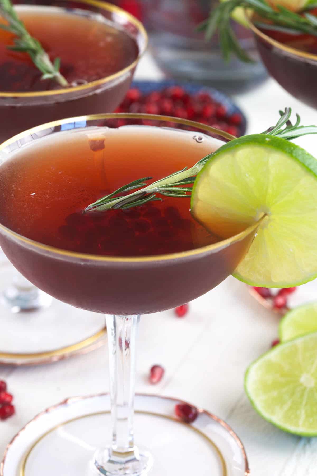 A pomegranate martini is garnished with herbs and a slice of lime.