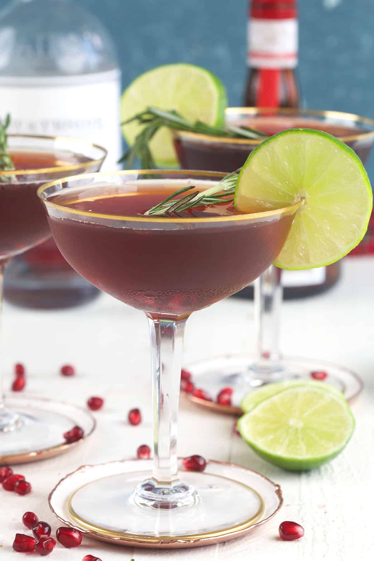 A pomegranate martini is presented next to scattered seeds and limes. 