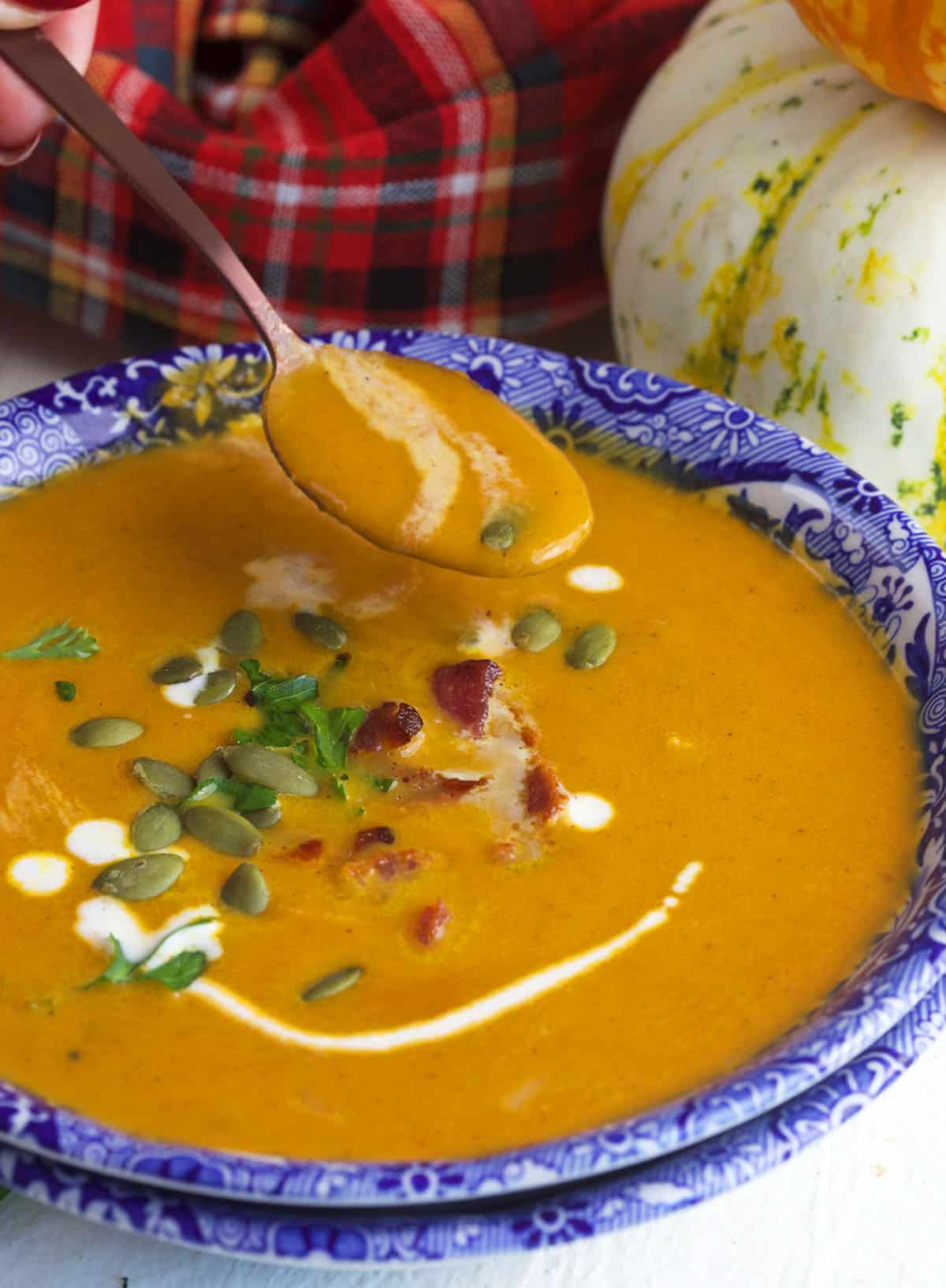 A spoon is held above a bowl full of pumpkin soup.