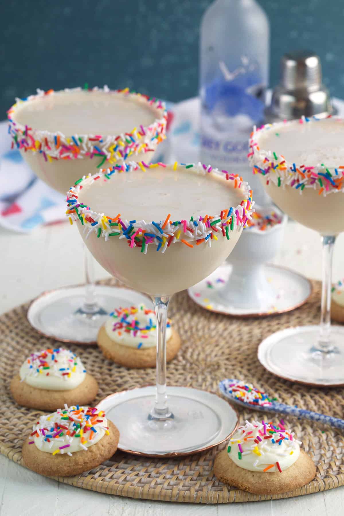 Three sugar cookie martinis are placed next to frosted sugar cookies. 