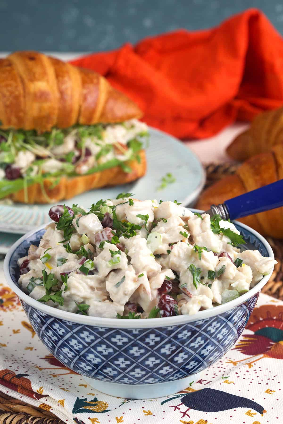 A bowl filled with turkey salad is placed in front of a sandwich. 